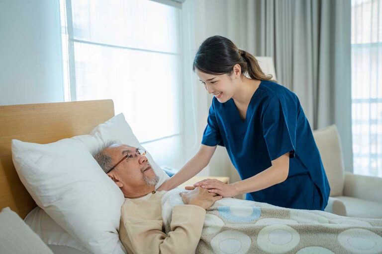 Caregiver speaks calmly with a senior resident seated in a bright assisted living room.