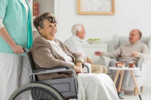 Older adult walking with a mobility aid along a bright assisted living hallway beside a supportive caregiver
